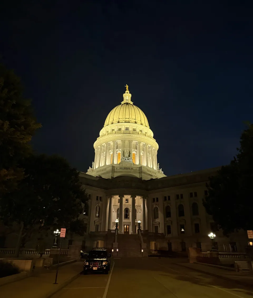 The floodlit dome of the Wisconsin State Capitol at night, seen from the foot of the building in downtown Madison